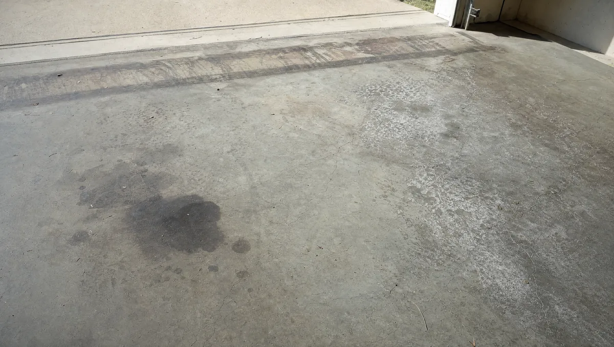Weathered concrete garage floor showing oil stains, surface dusting, spider cracks and hot tire marks